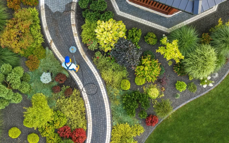 A service worker pressure washing and cleaning the pathway of the garden landscape of the house.